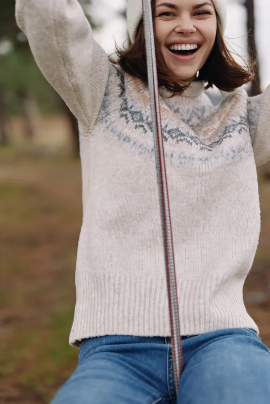 Girl on a swing in a park, wearing a knit sweater, smiling with joy on a sunny autumn day, a candid moment of outdoor happiness and carefree play.
