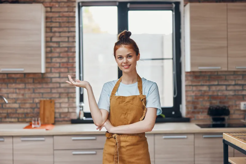 Домохозяйка в фартуке жестикулирует руками на кухне, домашняя работа, домашняя жизнь