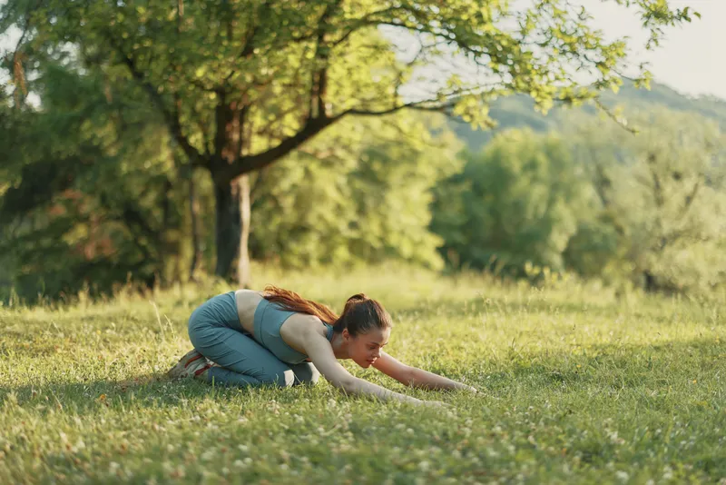 Young woman practicing yoga outdoors in a lush green field, showcasing serenity and mindfulness in a peaceful, natural setting