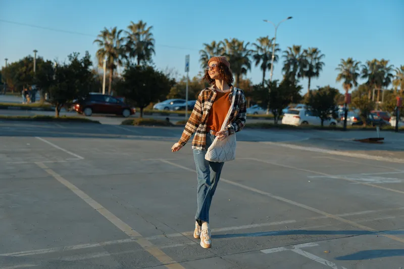 Woman walking parking casual sunlight golden authenticity candid lifestyle portrait in urban parking lot, relaxed fashion and mindful living with emotional storytelling and warm glow.