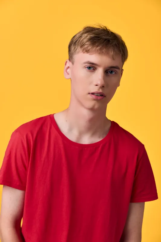 Young man in a red t shirt against a yellow backdrop, showcasing casual fashion with a clean pose and direct gaze for a studio lifestyle image, ideal for campaigns