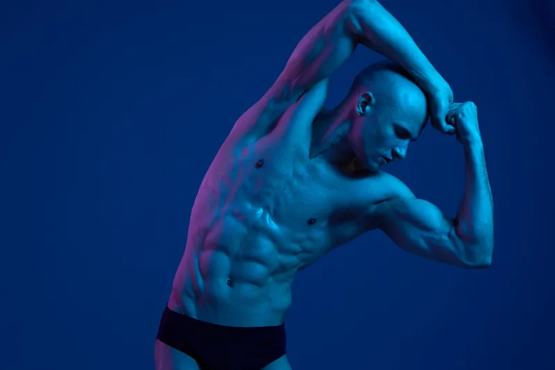 Athletic man posing in dramatic blue lighting, showcasing his impressive physique and strength. This striking image captures the essence of fitness and dedication.