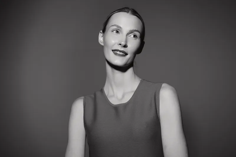 Young white woman with fair skin and dark hair smiles softly, looking aside on grey background. Concept of beauty and natural portrait.