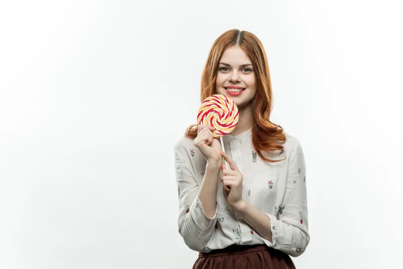 Женщина облизывает леденец, наслаждаясь сладкой конфетой на светлом фоне