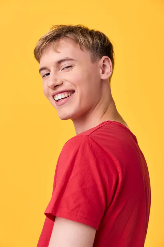 Smiling man in a red shirt against a vibrant yellow background, casual studio shot conveying confidence, upbeat mood, approachable vibe, and contemporary fashion in a bright setting