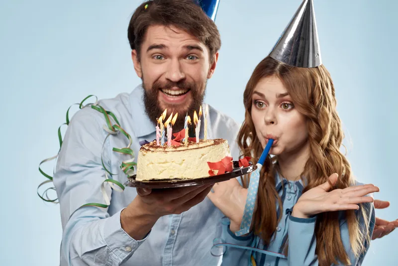 Мужчина и женщина празднуют день рождения с тортом и в колпаках на синем фоне