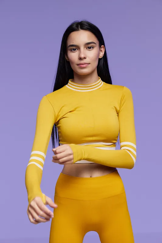 Sport fitness woman in yellow activewear stretching arms against purple background, focused and healthy young adult with long dark hair preparing for workout session.