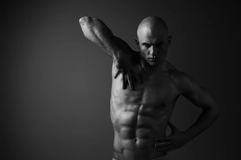Strong man posing creatively in black and white light, showcasing physical strength and dynamic movement. This artistic shot captures powerful emotion and artistry.