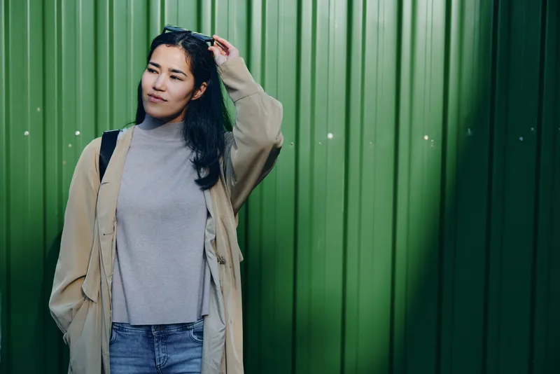 Woman, fashion, casual, outdoor, green, wall, denim, coat, sweater, urban style in a relaxed street scene against a green metal backdrop, soft light, natural tones, modern mood