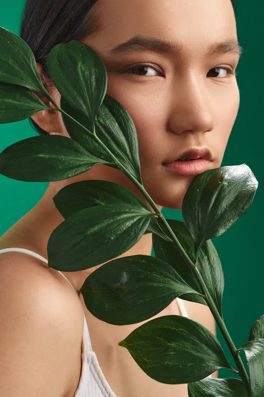 asian woman with leafy branch close up in beauty portrait style, serene expression and soft lighting create a calm, elegant mood that highlights natural skin tone and graceful detail.