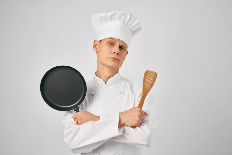 Повар работает на кухне, используя кухонную утварь и сковороду для приготовления еды