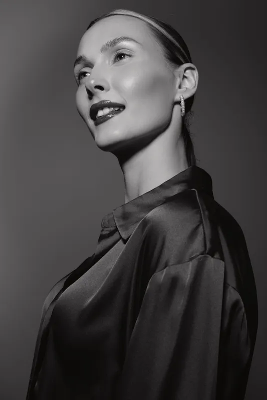 Elegant white woman with light skin poses in black silk blouse, looking sideways in black and white studio portrait. Concept for fashion, beauty, and classic style.