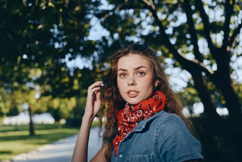 Lifestyle woman in modern boho-western denim street style with red bandana, captured in natural light and film color creating warm, casual outdoor atmosphere.
