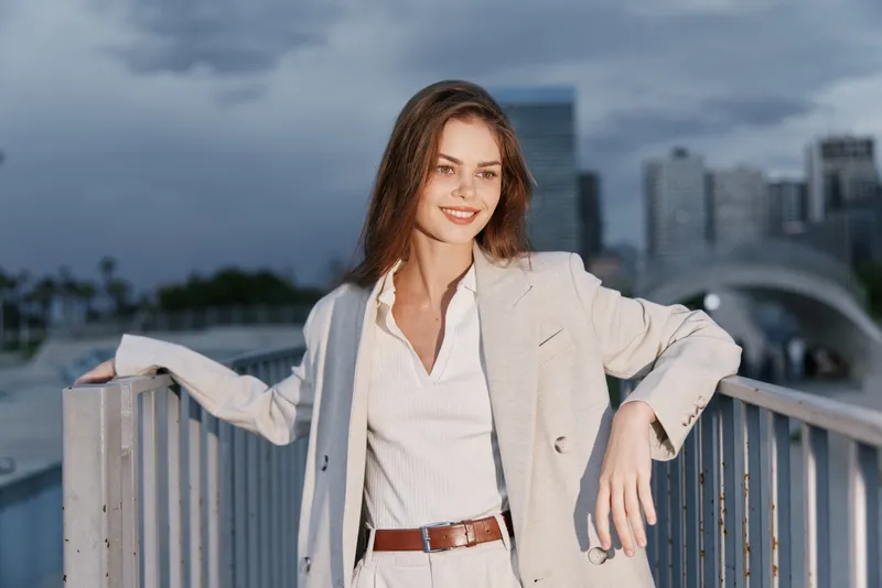 confident woman in beige suit smiling outdoors with cityscape background, business attire, urban style, professional woman, daylight
