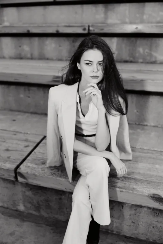 Black and white portrait of a pensive woman in white business suit sitting on wooden steps expressing thoughtful emotions