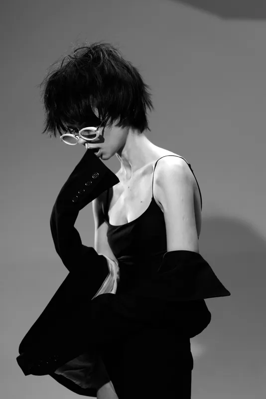 Black and white portrait of a stylish woman wearing glasses and elegant clothing with a contemplative expression.