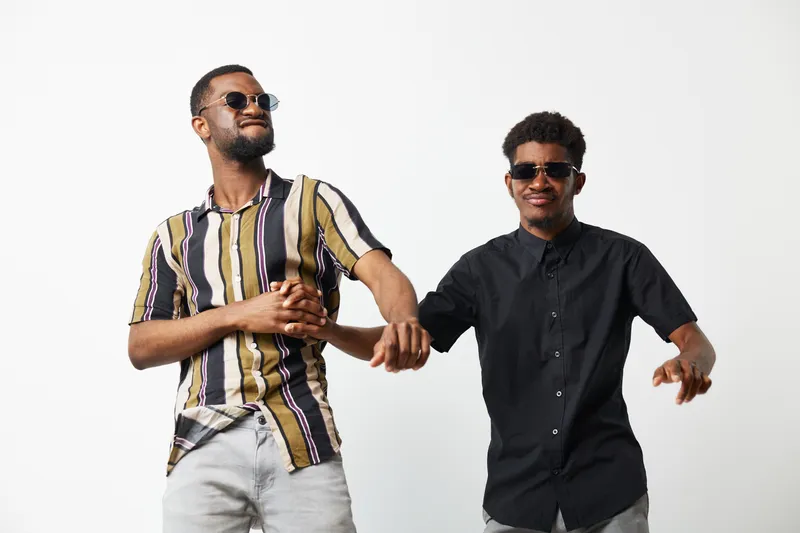 Stylish black men enjoying a fun moment together, showcasing their vibrant fashion choices and joyful expressions in a bright, energetic setting.