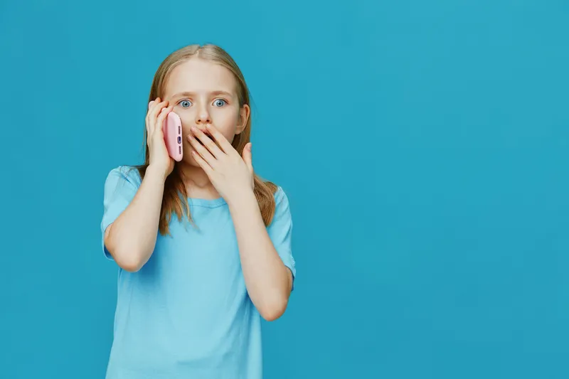 Surprised girl talking on smartphone with blue background, expressing shock and curiosity, dressed in casual light blue t shirt
