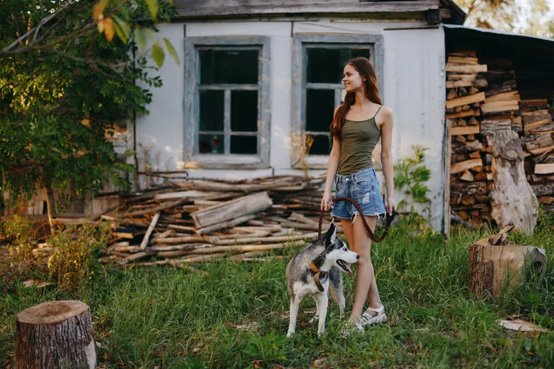 Женщина и её хаски весело играют на улице в парке среди деревьев, улыбаясь, показывая зубы, во время осенней прогулки со своим питомцем