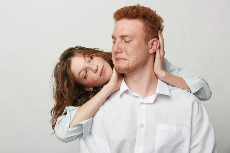 Young couple in casual clothes embraces tenderly, woman gently holding man's neck. Intimate moment of affection and connection on neutral background, concept of love and relationships.
