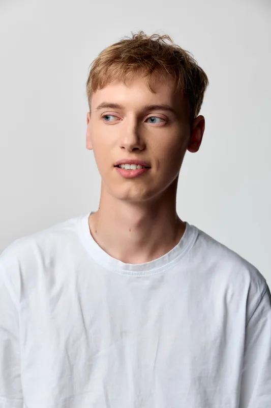 Young man in white t shirt and casual attire under studio lighting against a neutral background, head and shoulders pose with a soft expression, delivering a modern, versatile look for lifestyle and