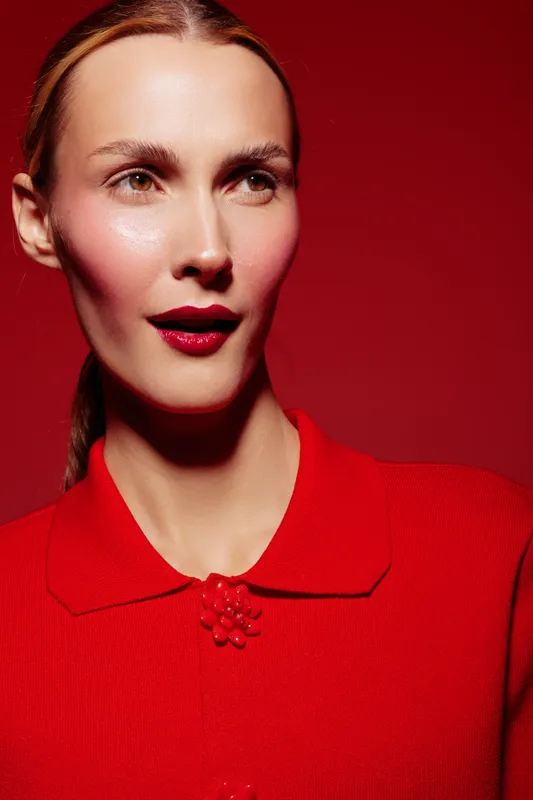 Portrait of a woman with red lipstick and red outfit against red background. Studio lighting highlights her smooth skin and elegant expression. Concept of fashion and beauty.