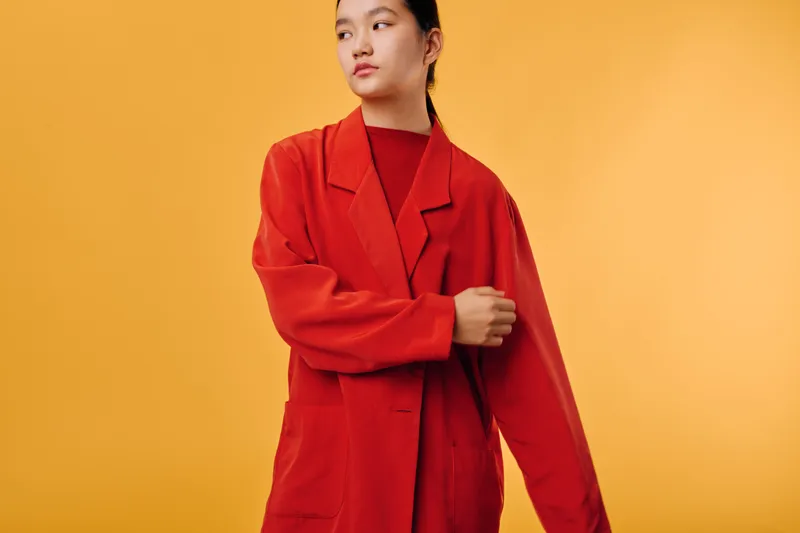 Young woman in red oversized blazer posing sideways on yellow background with serious expression fashion modern casual style minimal studio portrait female model.