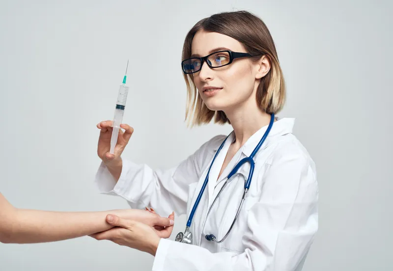 Женщина-врач в медицинском халате делает укол пациенту