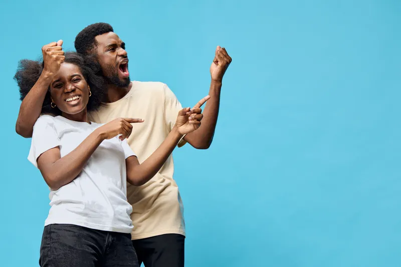 Happy couple celebrating success with joyful expressions against a bright blue background, showcasing emotions of happiness, teamwork, and excitement