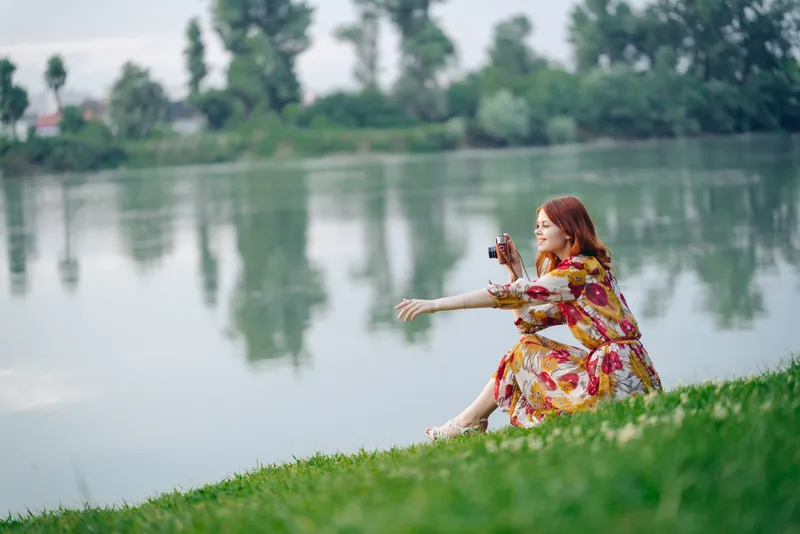 Симпатичная женщина в платье на природе с фотоаппаратом в руках