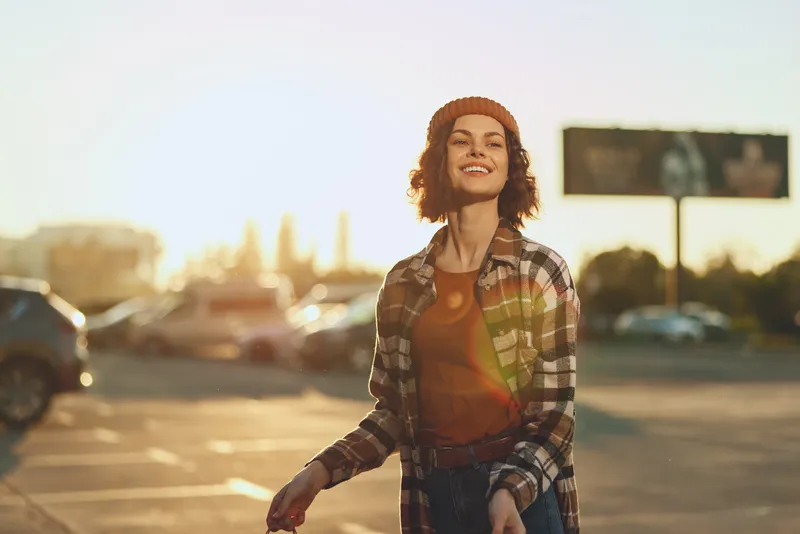 Woman smile golden candid urban parking casual beanie portrait showing authenticity and mindful living, emotional storytelling of a carefree city moment with warm sunlit glow.