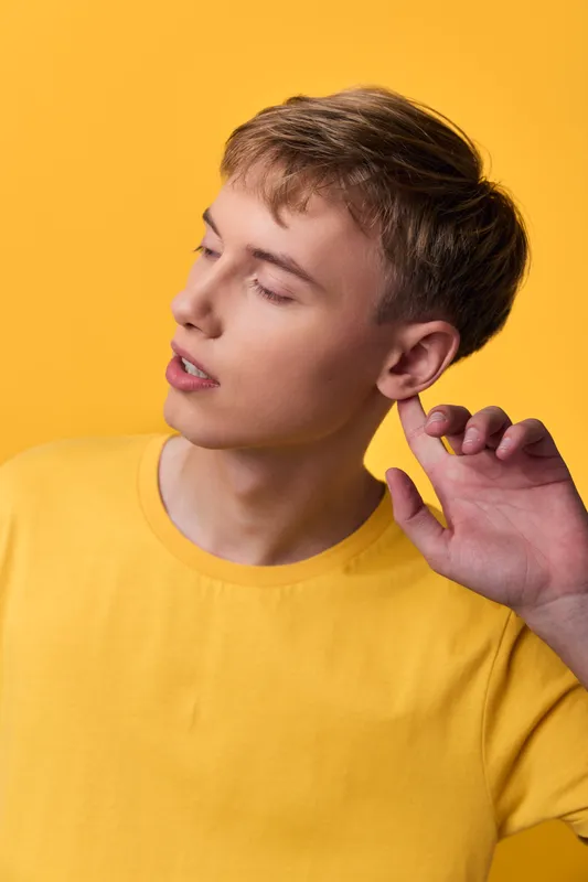 Young man side profile with a yellow shirt gazes away, showcasing thoughtful mood, clean studio lighting, and bold color for a modern casual fashion shot