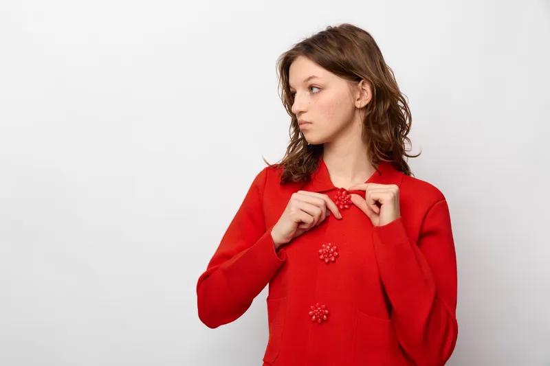 Young woman in red sweater looks to the side with thoughtful expression. Studio portrait on white background. Concept of fashion, casual style, and contemplation.