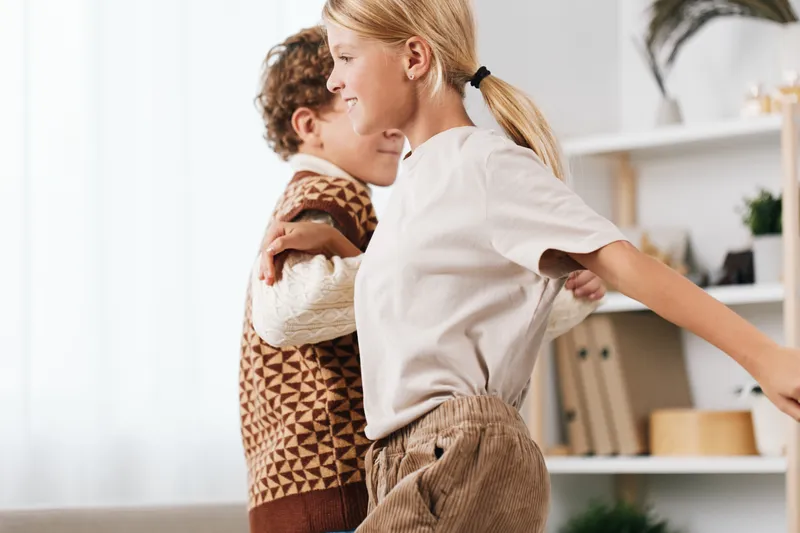 Authentic moment of children at play, capturing a school themed lifestyle in a warm home setting as kids dance and share a hug, reflecting joy and everyday learning.