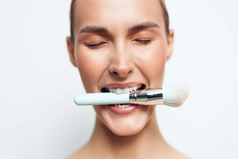 Young woman with a makeup brush studio portrait playful expression and bold makeup
