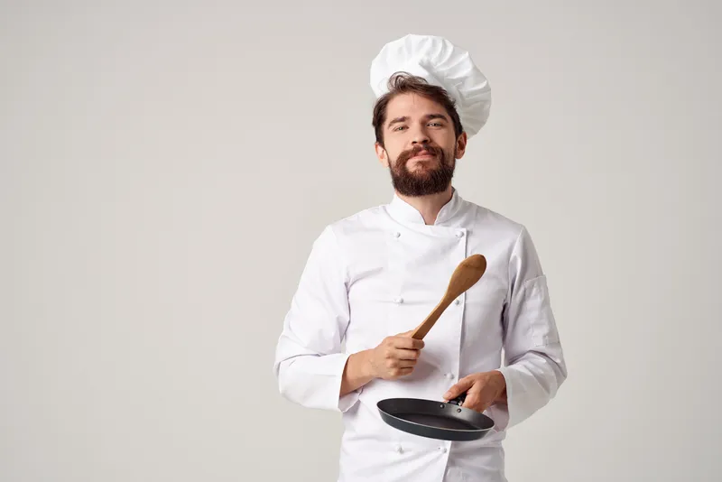 Веселый шеф-повар мужского пола работает на кухне, занимаясь приготовлением пищи профессионально