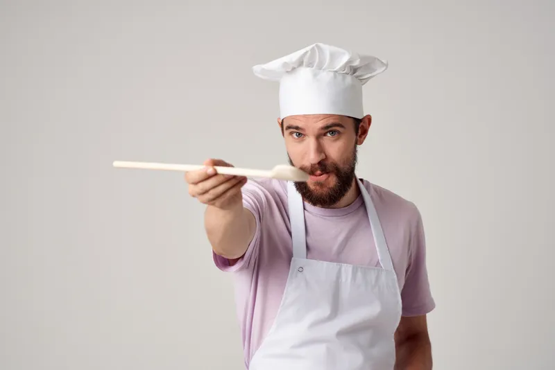 Шеф-повар в униформе работает с кухонной утварью, занимаясь приготовлением пищи