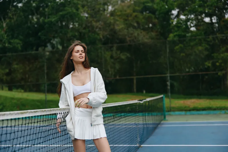 Young woman playing tennis outdoors, wearing sporty attire a white tank top and a skirt, showing determination on a sunny day