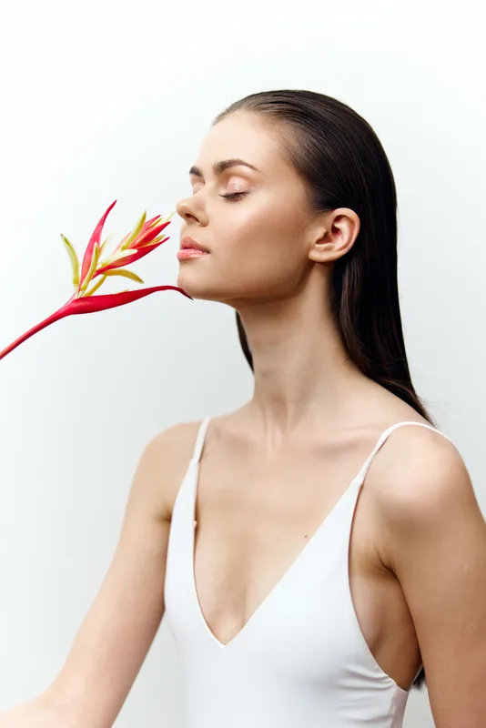 Красивая модель в белом купальнике взаимодействует с ярким тропическим цветком, отражая красоту и безмятежность в минималистичной композиции