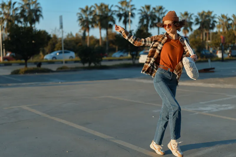 Woman joyful fashion moment in urban parking lot at golden hour, candid lifestyle portrait conveying authenticity, mindful living and emotional storytelling with warm glow.