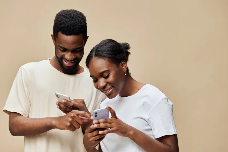 A joyful couple engaged with their smartphones, showcasing technology s role in modern relationships, with warm beige backdrop enhancing their smiles