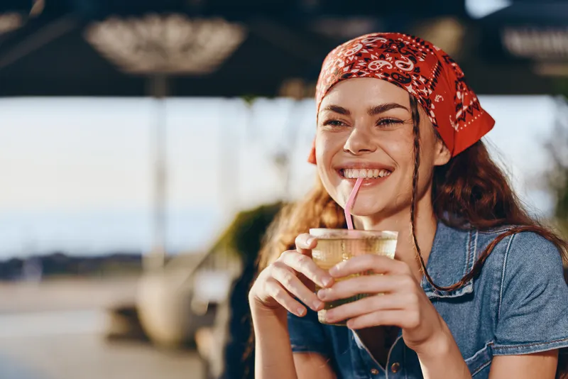 smiling woman enjoying cold drink outdoors with red bandana and casual denim shirt in sunny day relaxed and happy summer vibe