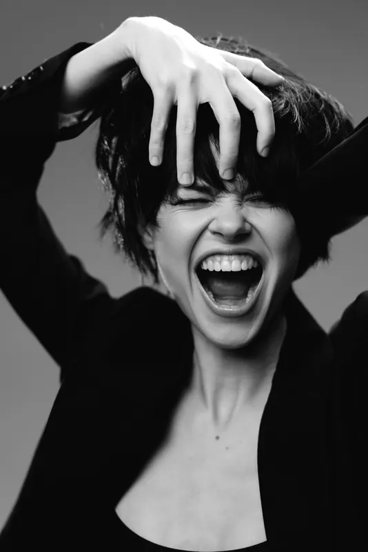 Black and white portrait of excited woman screaming with hands in hair, expressing strong emotion and passion in dramatic style.