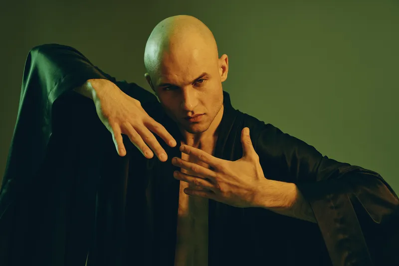 A striking man showcasing expressive hand gestures, wearing a black robe. The artwork features a unique color light effect, enhancing the overall dramatic atmosphere.
