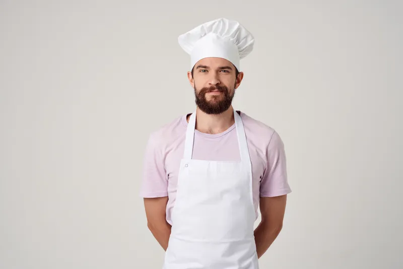 Бородатый мужчина в белом фартуке готовит на кухне ресторана