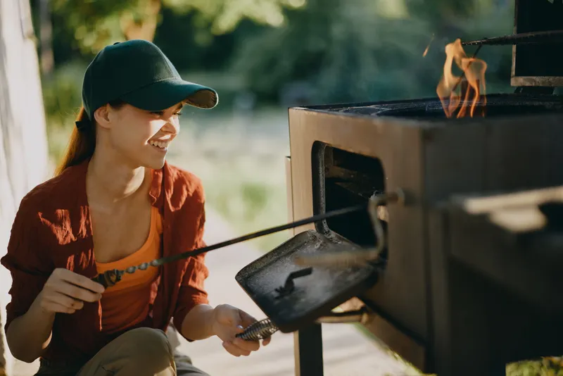 Young woman with a bright smile grilling outdoors in casual attire, showcasing a joyful moment in nature with vibrant colors and summer vibes