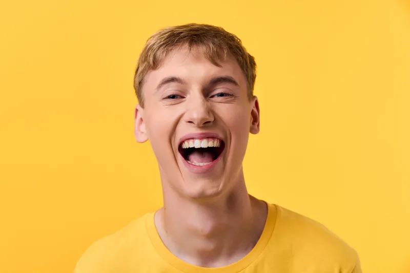 Bright yellow background, a wide smile and loud laughter from a young man in a yellow tee, conveying energy, happiness, and a positive mood for lifestyle or advertising