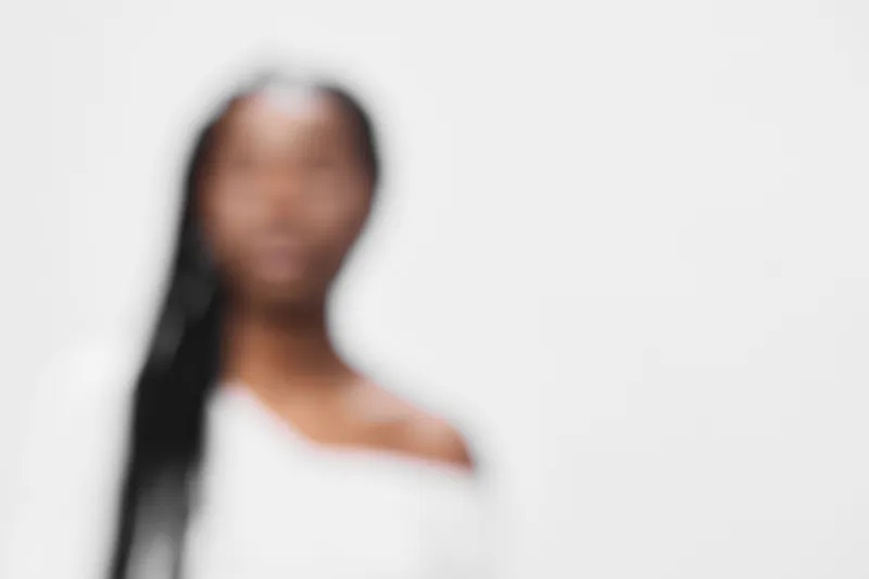 Blurred portrait of a stylish woman with long braids in an off shoulder white top, conveying elegance and confidence in a minimalistic white background