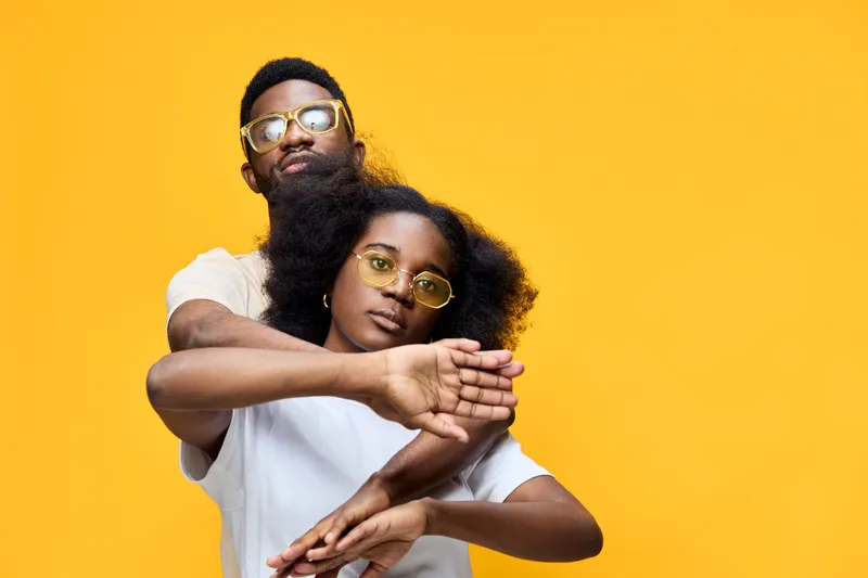 Stylish young couple with sunglasses posing against a vibrant yellow background, showcasing love and confidence with a playful vibe, perfect for fashion and lifestyle concepts