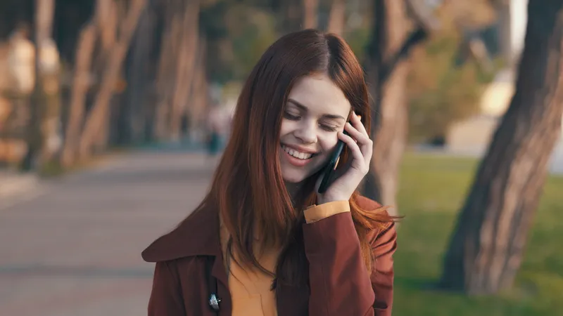 Симпатичная женщина в пальто с телефоном в руке гуляет по парку, отдыхая